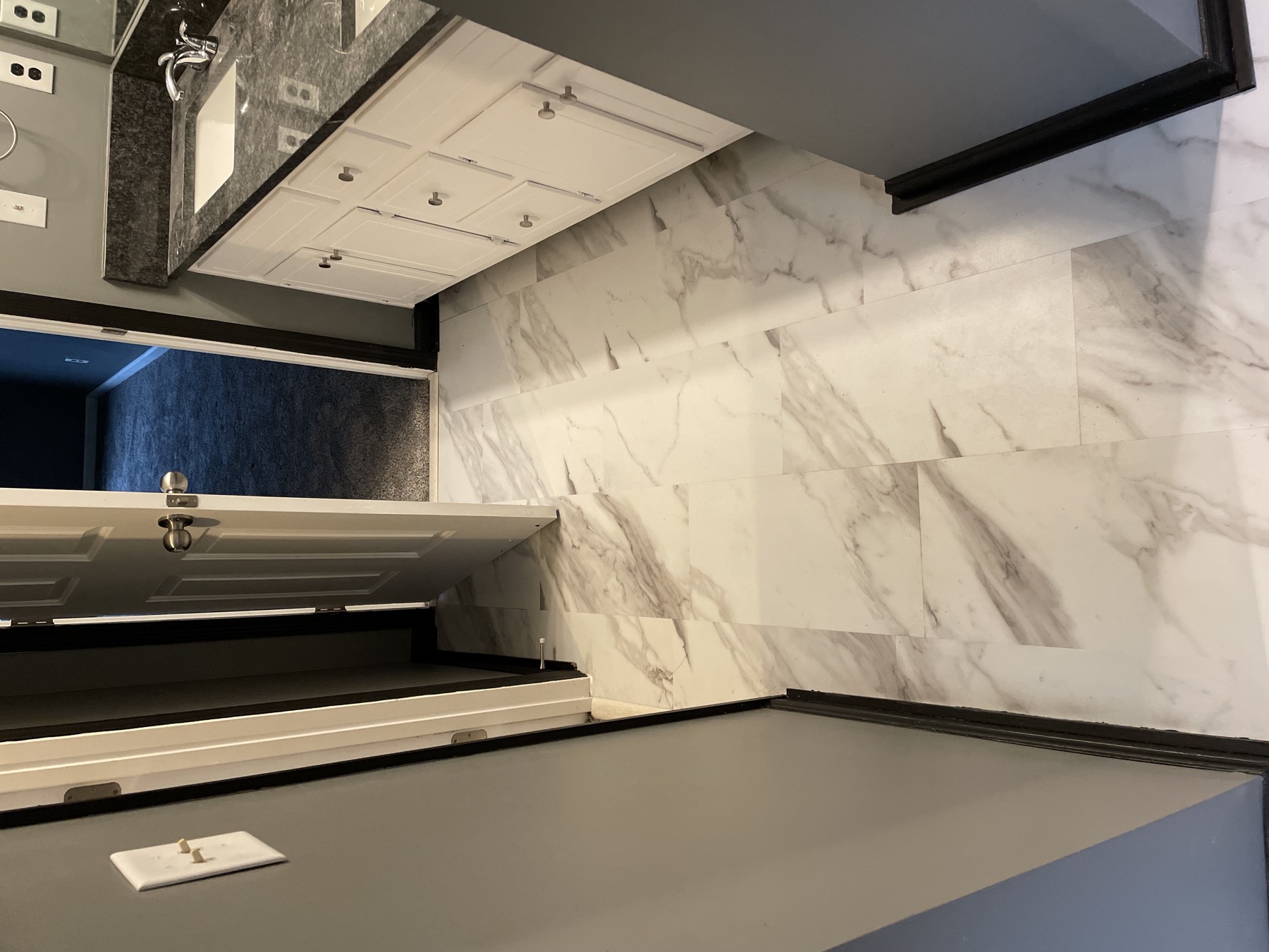 Bathroom with marble-look tile flooring and dark baseboard trim