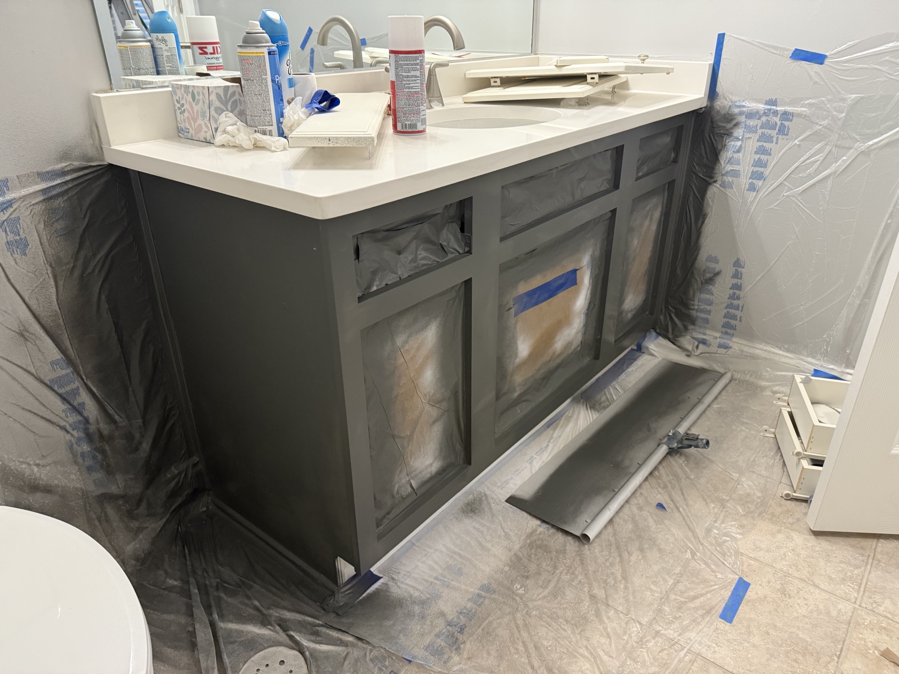 Bathroom vanity being spray-painted charcoal, masked with plastic